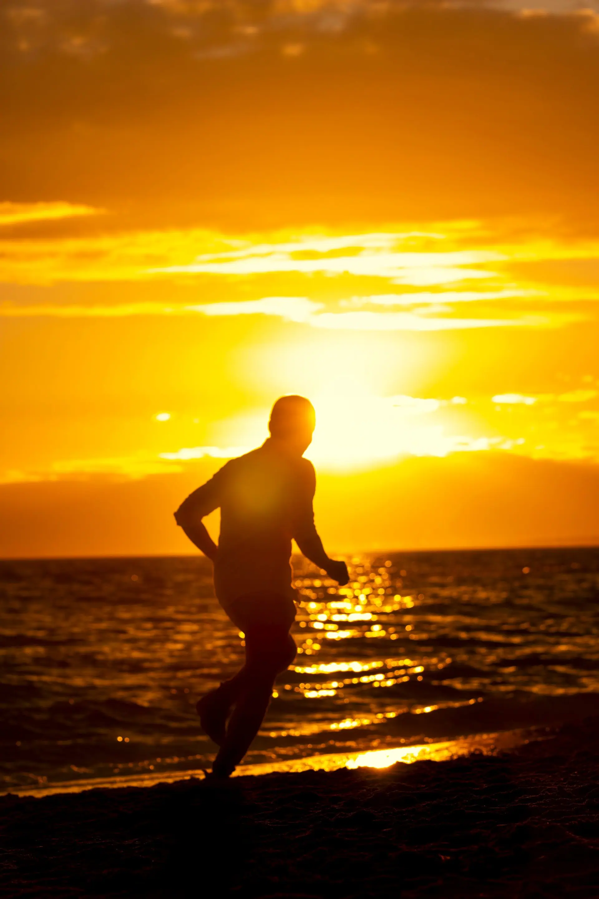 Homem correndo na beira do mar com o sol dourado se pondo ao fundo